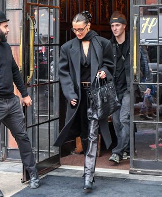 Bella Hadid wears a black wool coat, black blouse, black leather pants, black boots, and black hermes bag.