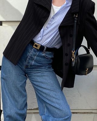 NYC woman wears a Saint Laurent black leather belt with gold hardware, black blazer, a blue button-down, and jeans.