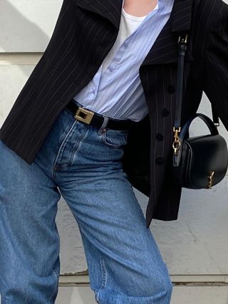 NYC woman wears a Saint Laurent black leather belt with gold hardware, black blazer, a blue button-down, and jeans.