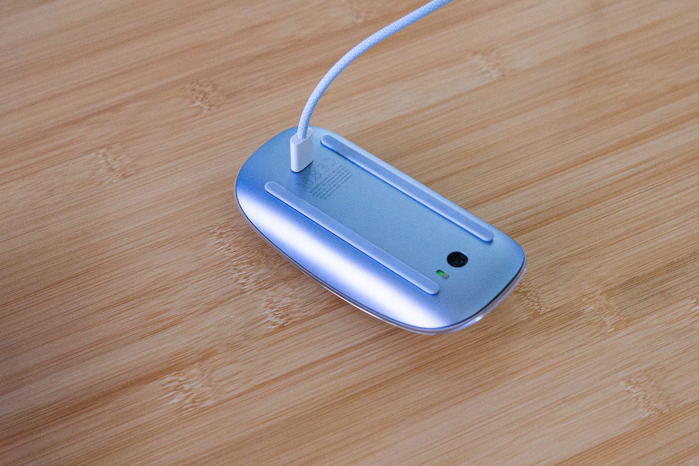 Picture of a Magic Mouse with USB-C laying upside-down with a charging cable plugged into it.