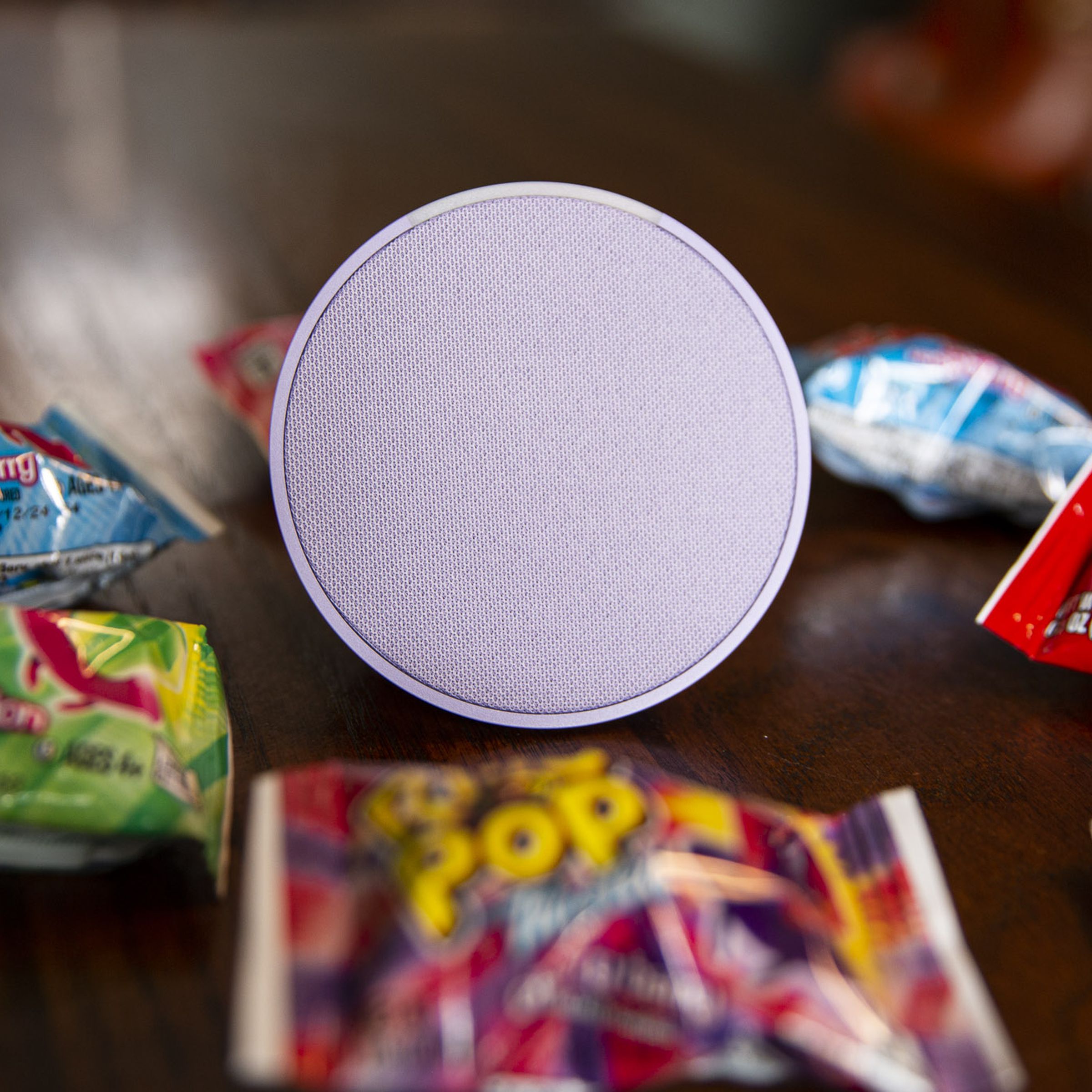 A purple Echo Pop smart speaker on a table surrounded by Ring Pop candy.