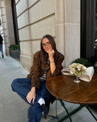 Emma wears a brown blazer, strip shirt, blue jeans, white socks, and black ruched loafers.