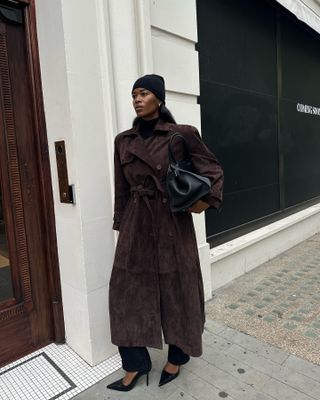 Marilyn Nwawulor-Kazemaks in a black hat, brown suede jacket, and black trousers.