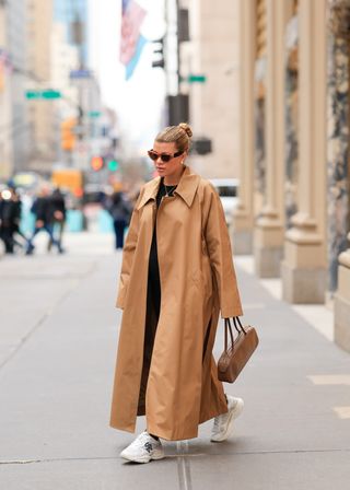 Sofia Richie Grainge walking on a city sidewalk wearing sunglasses, a tan coat, white sneakers, and the Khaite Simona Bag.