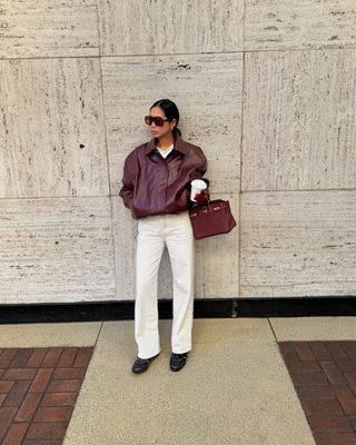 Woman wearing burgundy leather jacket and white jeans.