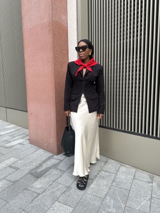 Woman wears red scarf, black blazer and cream skirt