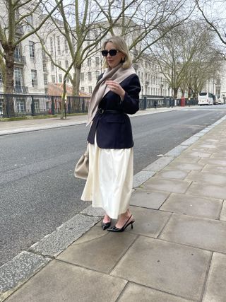 Woman wears black blazer, cream skirt and beige scarf