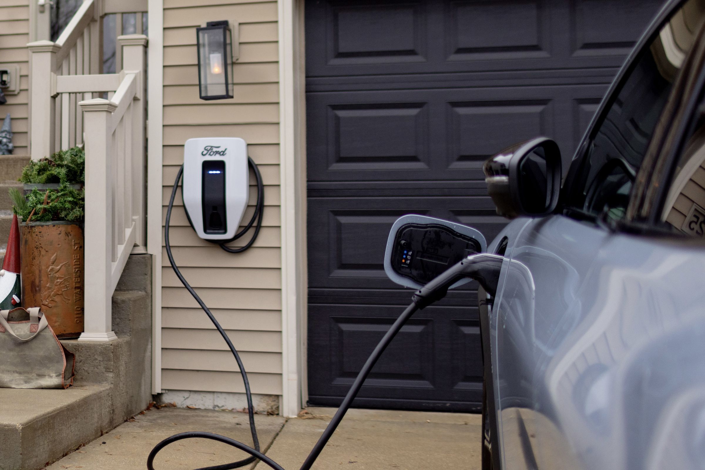 front of house with Ford branded charger next to garage door and a blue mach-e plugged in.