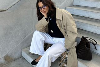 woman in navy sweater, white jeans, and trench coat