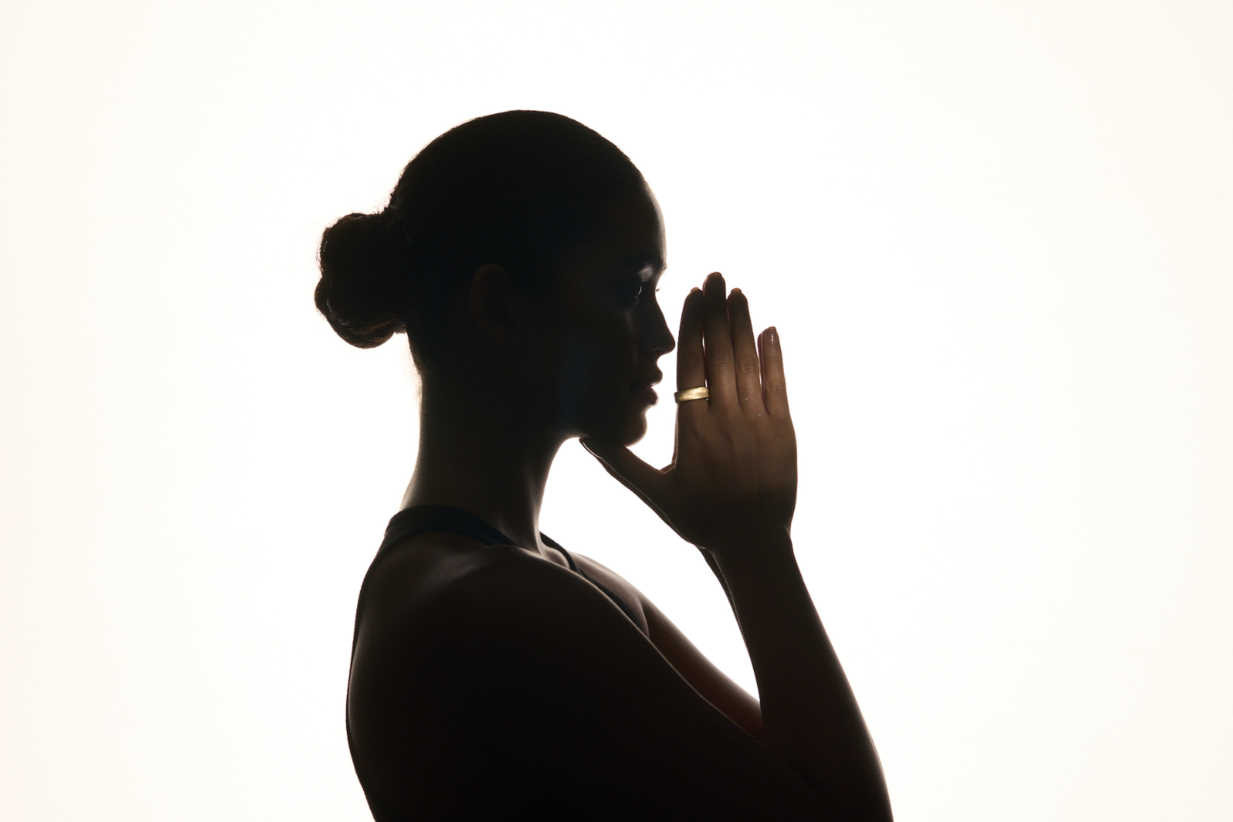 Artsy picture of model in dark silhouette, the Ultrahuman Rare smart ring in dune illuminated on her finger.