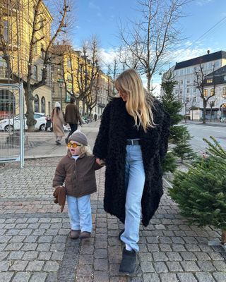 Jeannette wears a black fur coat, black top, black belt, blue puddle jeans, and black ugg boots.